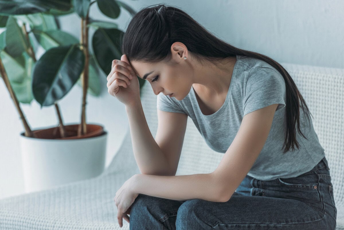 Frustrated young woman in depression sitting on couch and looking down