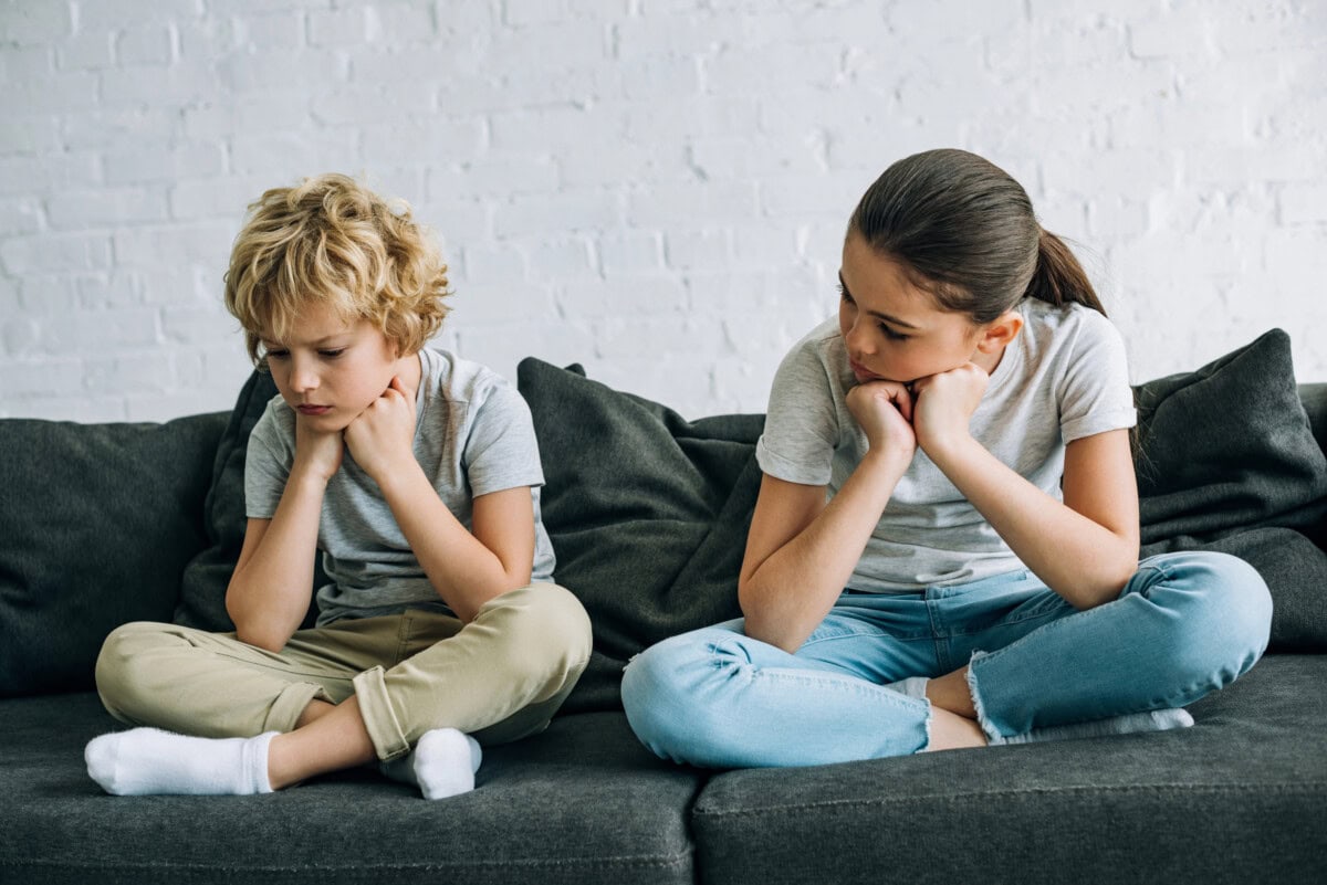 Two sad kids sitting on sofa in living room