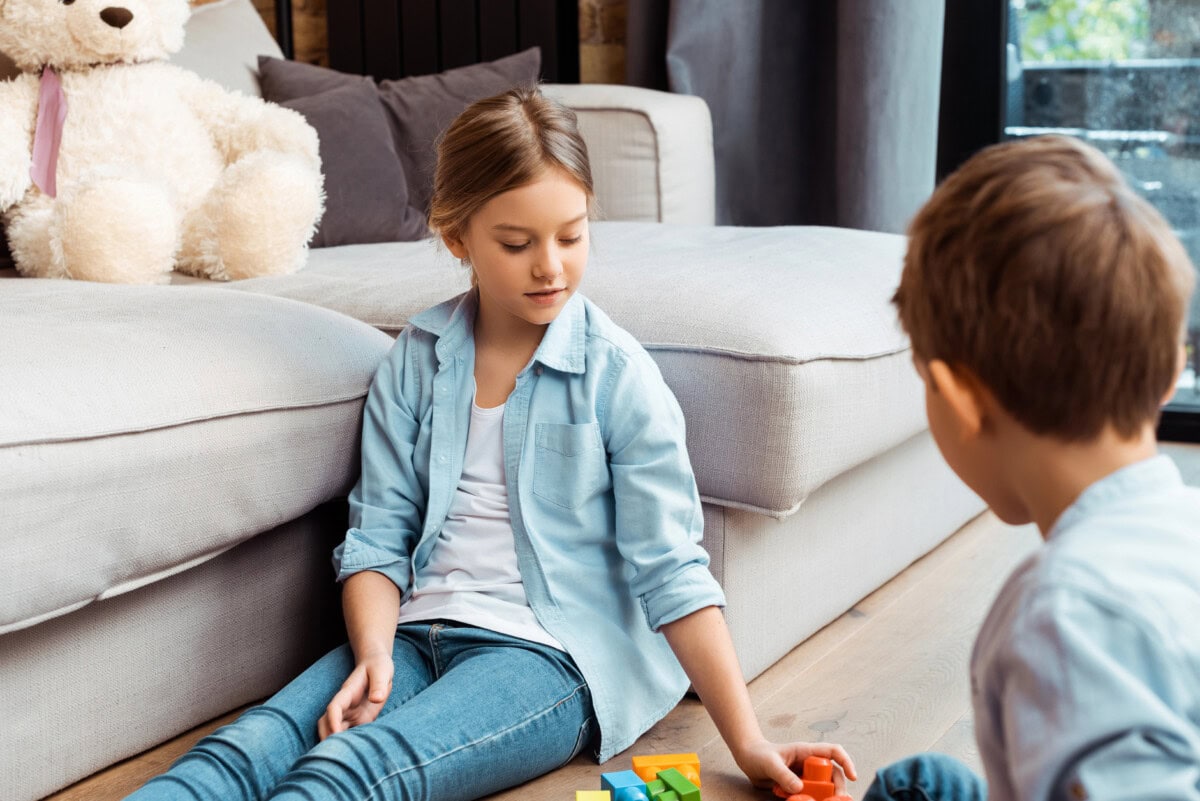 Selective focus of sister sitting on floor near brother and building blocks