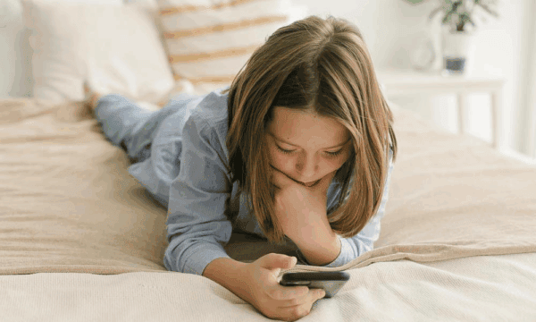 Schoolgirl 8-9 years old lies on her bed looking at her phone and texting message in mobile app on smartphone Photo